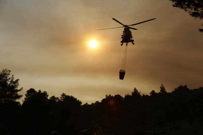 A firefighting helicopter approaches a lake to load water, as it participates in an operation against a wildfire in northern Athens