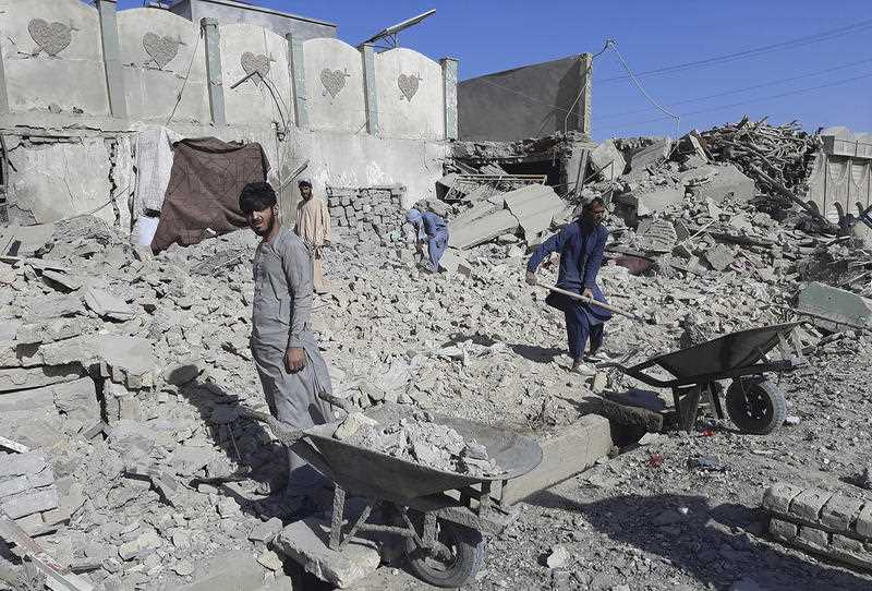 2 Afghan men with wheelbarrows inspect a damaged building after airstrikes in Lashkar Gah city of Helmand province, south of Kabul