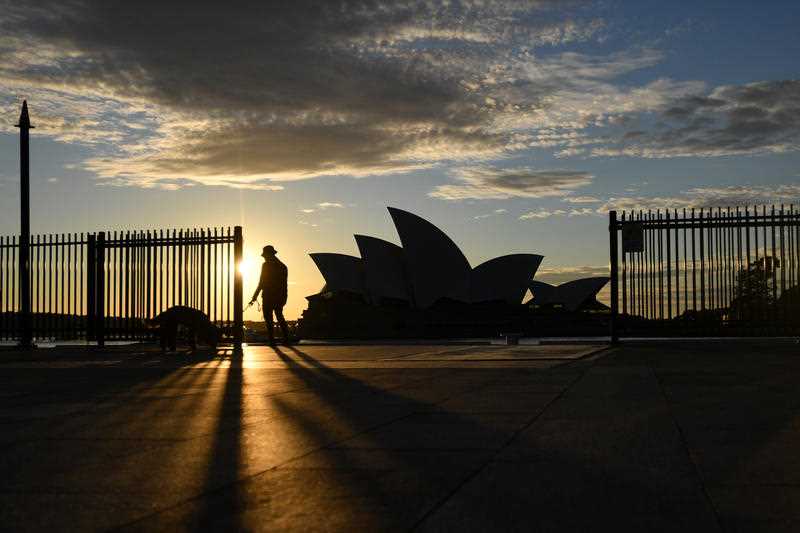 Silhouette of one lone pedestrian walking their dog near the Sydney Opera House at sunrise