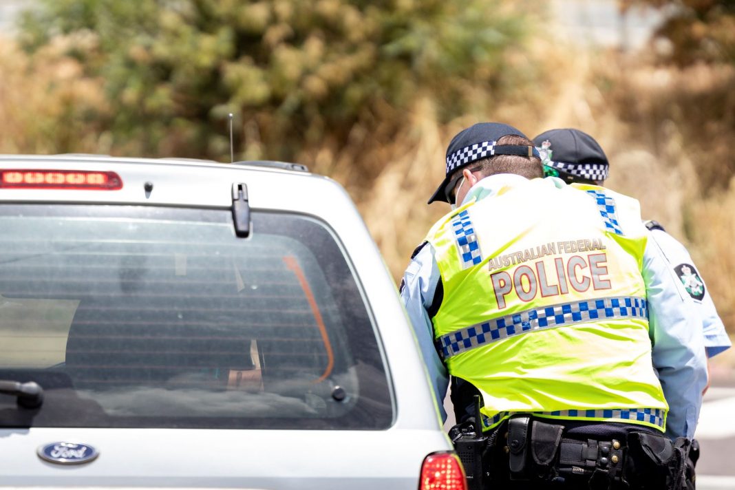 Two police officers in hi-viz vests checking cars entering the ACT at the NSW border