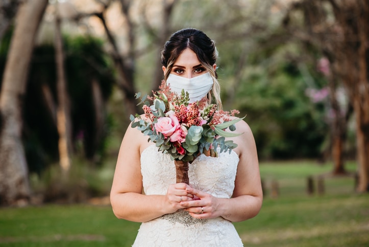 Bride with face protection mask holds bouquet with hands