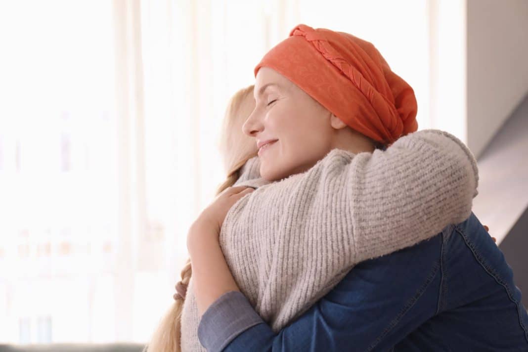 Female cancer patient wearing a headscarf hugging another woman