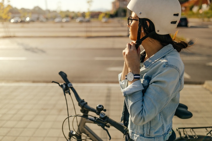 Young woman putting on her helmet, preparing for the bike ride
