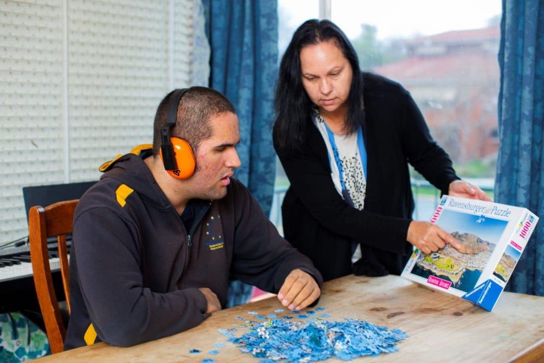 female carer helping a young man with disability to do a jigsaw puzzle