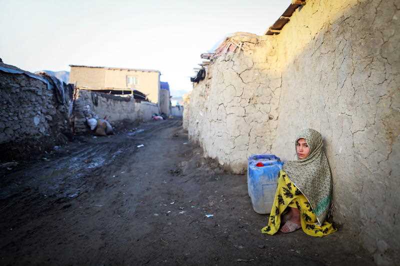 An internally displaced Afghan girl waits with water containers to be filled from a tanker outside of her temporary shelter in Kabul, Afghanistan