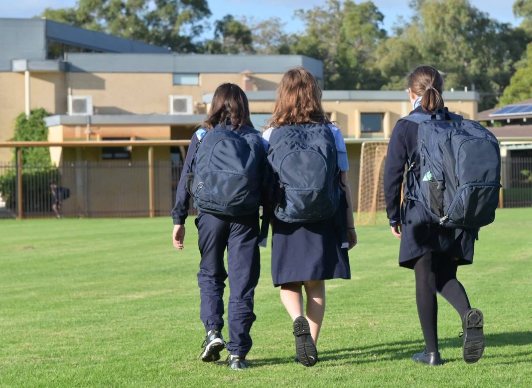 three school students with backpacks walking in school grounds