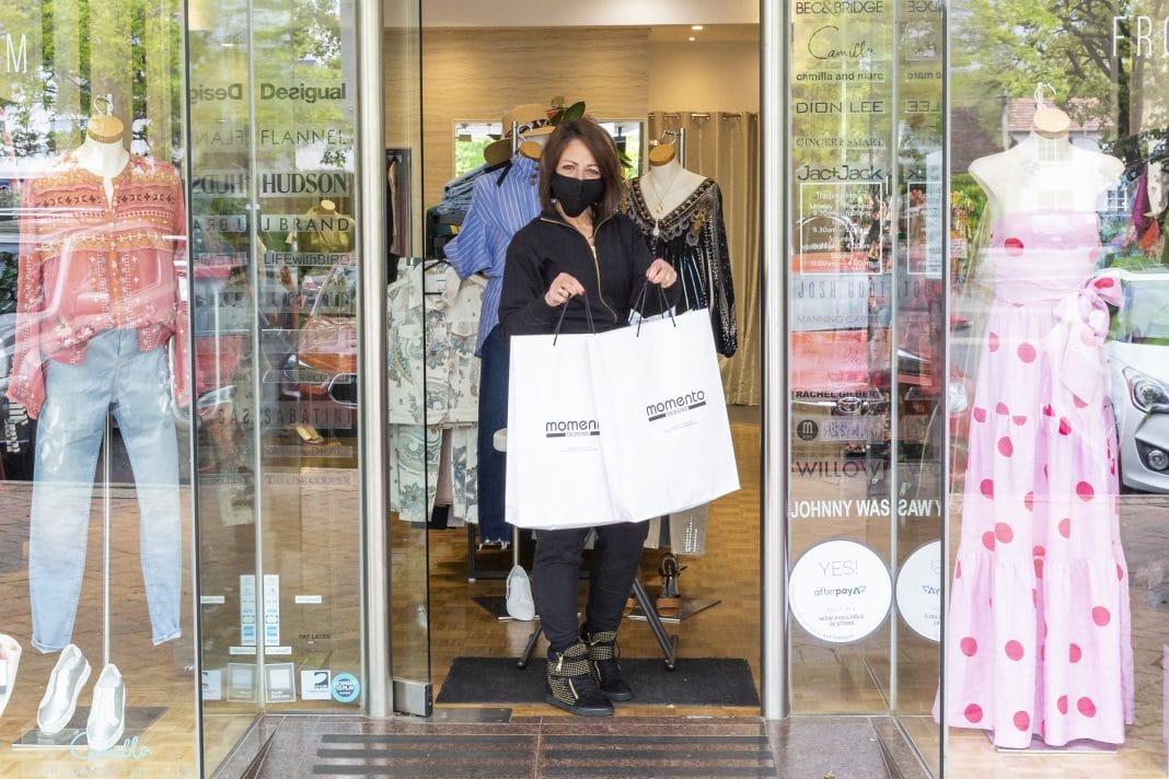 woman wearing face mask is seen holding shopping bags at entry to fashion boutique