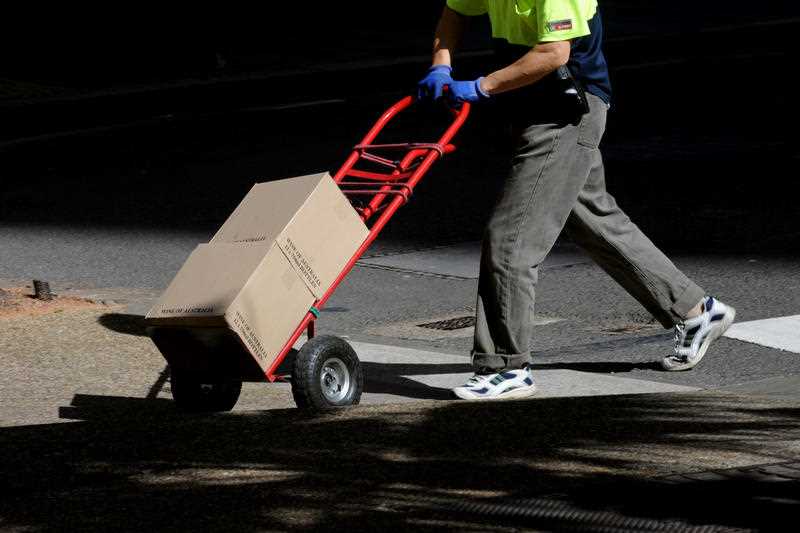 A delivery worker wheels a trolley with two cartons on it
