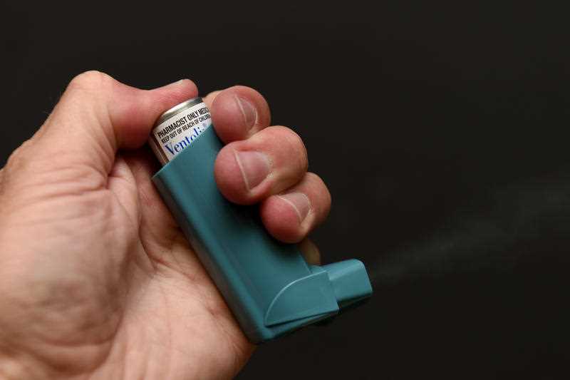 A hand holds a canister of Ventolin, also known as an asthma puffer