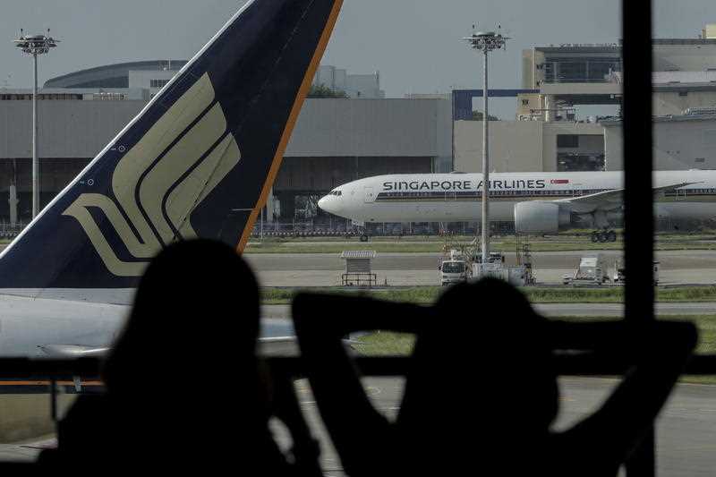 Two women are silhouetted against the Singapore Airlines logo at Changi Airport's Terminal 1 in Singapore