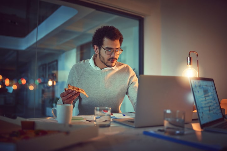 Shot of a young designer eating pizza while working late in an office