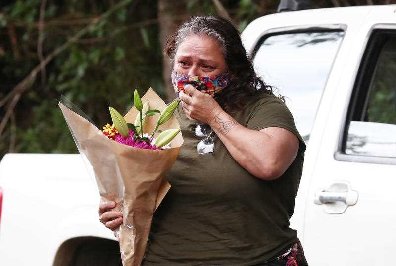 A member of the public reacts while holding a bouquet of flowers outside the home where twin four-year-old girls died following a house fire, in Goonengerry, west of Byron Bay, Sunday , November 7, 2021