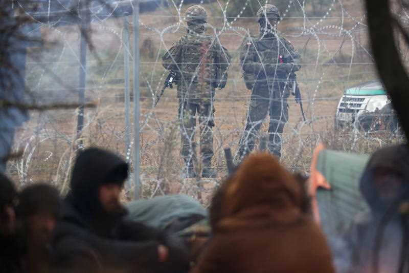 migrants at their camp at the Belarus-Polish border in the Grodno region, Belarus, 10 November 2021, as Polish servicemen keep guard behind a barbed wire fence