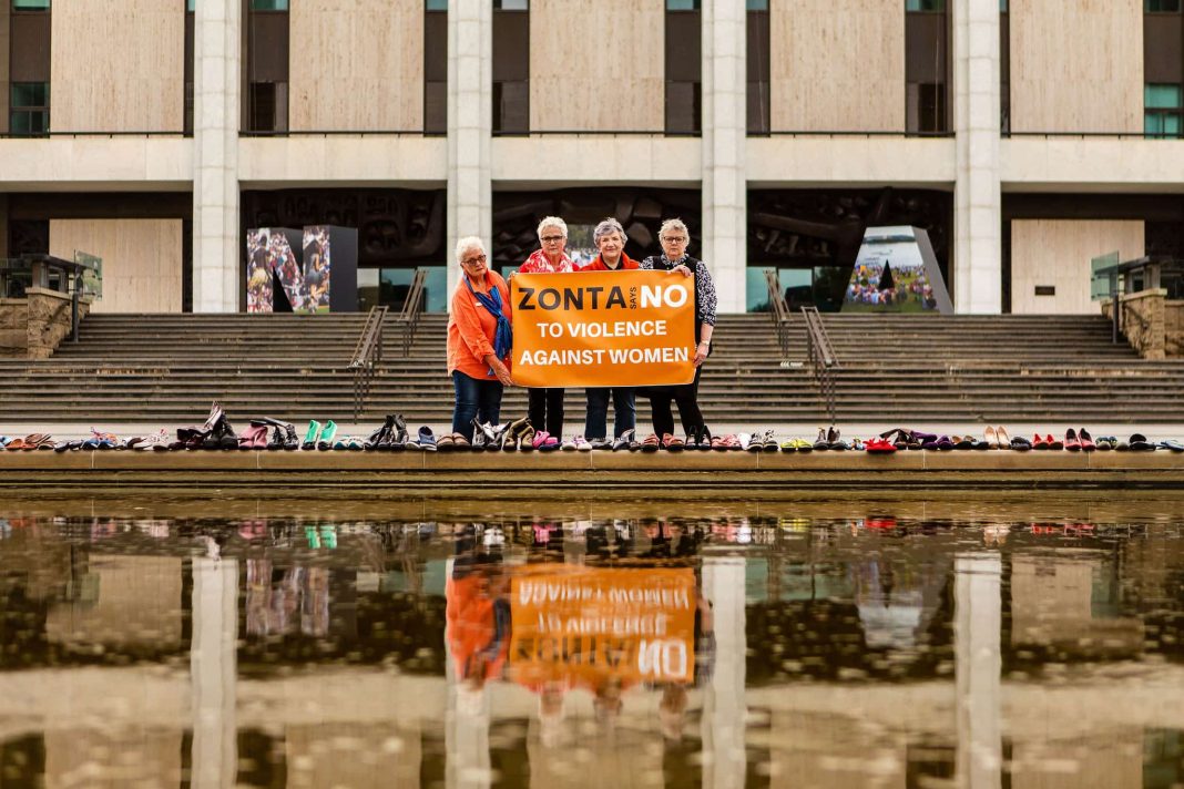 4 women dressed in orange with 'Say No to Violence' placards and 38 pairs of shoes, one for each victim of domestic violence in Australia in the past 12 months, out front of the National Library of Australia