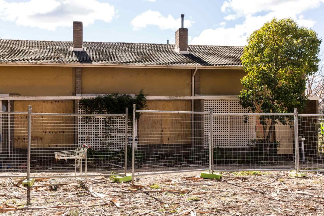 Derelict public housing units with abandoned shopping trolley behind fence