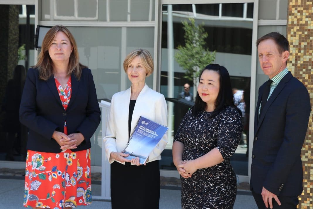 Three professional women, one of whom is holding a report on sexual assault in the ACT, and a man in a suit stand outside the ACT Legislative Assembly building in Canberra