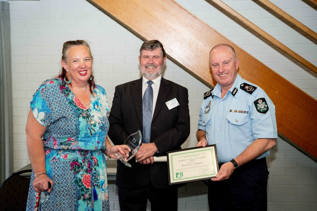 female Neighbourhood Watch volunteer receiving an award from ACT Chief Police Officer as male Neighbourhood Watch president looks on