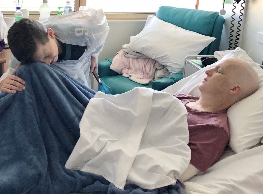 sick male cancer patient in bed with young son crying at his bedside
