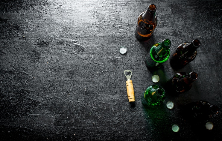 Open glass beer bottles and opener. On black rustic background