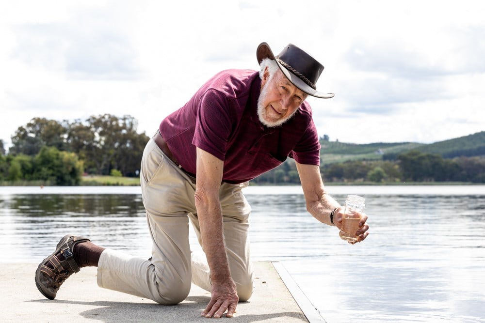 elderly man wearing hat taking water quality sample from Lake Burley Griffin in Canberra