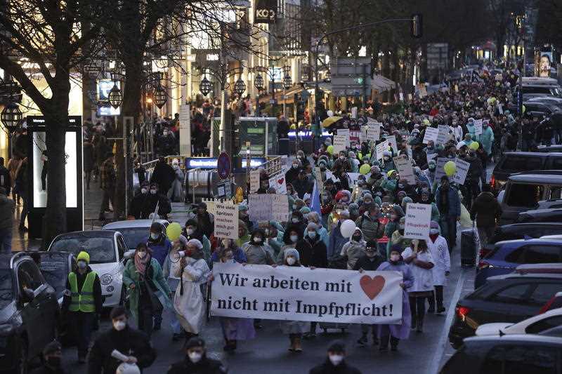 People walk down Konigsallee with a sign reading 'We work with heart not compulsory vaccination! 'as they demonstrate against the government's coronavirus measures, in Duesseldorf, Germany, Saturday, Jan. 29, 2022.