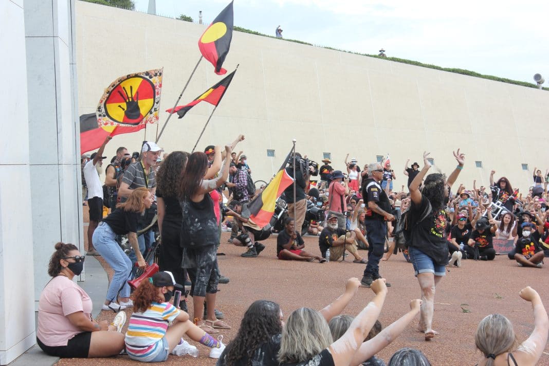 people protesting with Aboriginal flags outside Australian Parliament House in Canberra on 26 January 2021