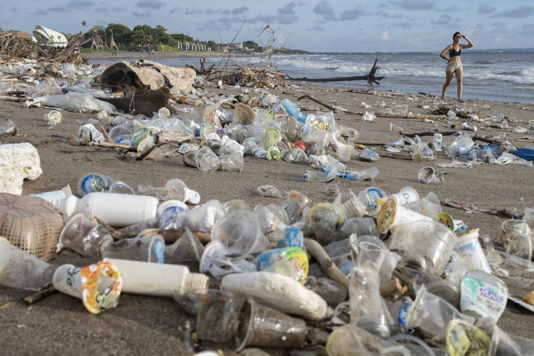 Tourists walk along a beach covered in piles of debris and plastic waste brought in by strong waves at a beach in Canggu, Bali, Indonesia, 13 December 2021
