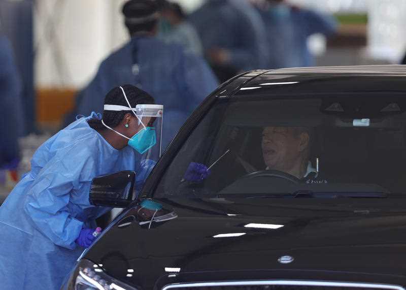 A health staff member is seen administering a PCR test as members of the public queue in their cars at a drive-through COVID-19 testing site in Melbourne