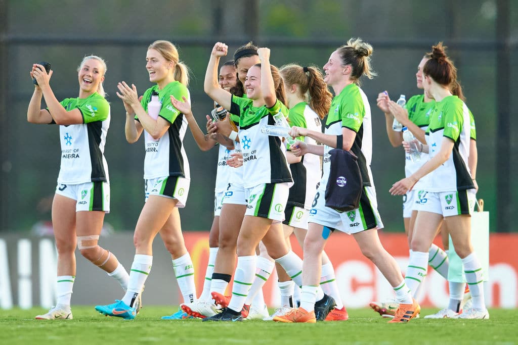Nine smiling female footballers from Canberra United are seen celebrating after their first win of the season