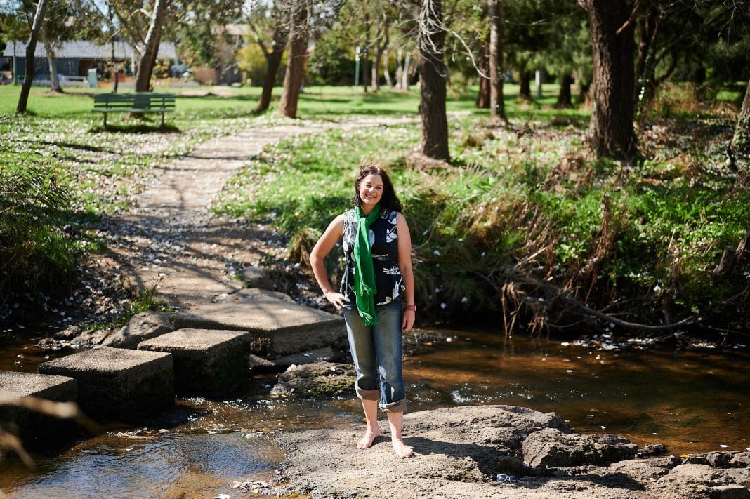 ACT Greens MLA Jo Clay is seen standing barefoot near a muddy stream in a Canberra park