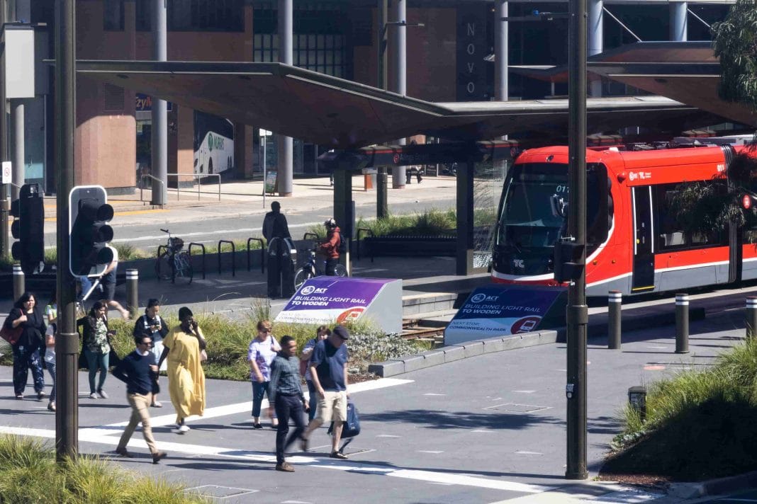 pedestrians are seen crossing a major intersection at traffic lights near Light Rail stop in Canberra City