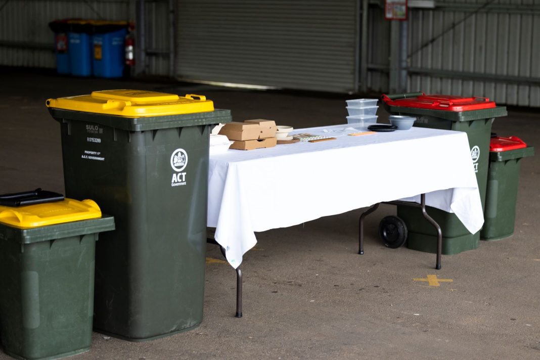 biodegradable takeaway food containers on a table beside yellow lidded wheelie bins for recycled materials