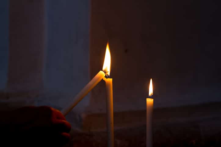 Lighting a church candle (one of three); hand barely visible in the foreground. Lots of copy space on the dark background.
