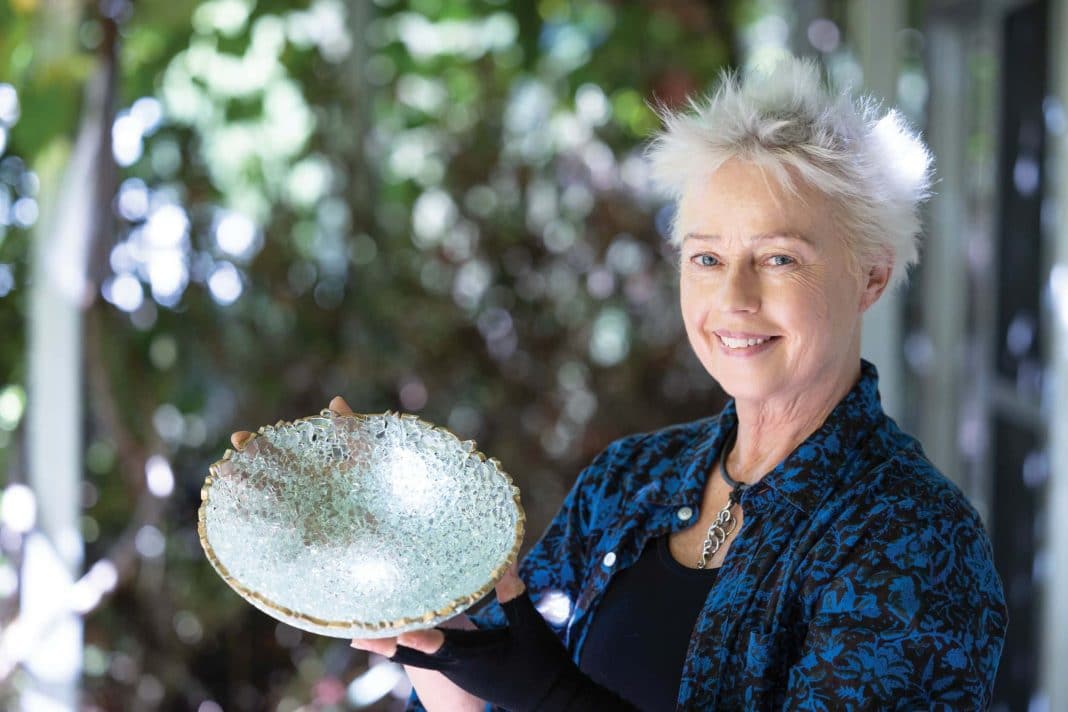 smiling artist holding a glass bowl she makes from shattered glass