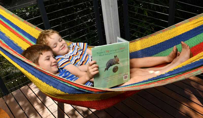 Two young brothers are seen lying in a hammock reading a storybook