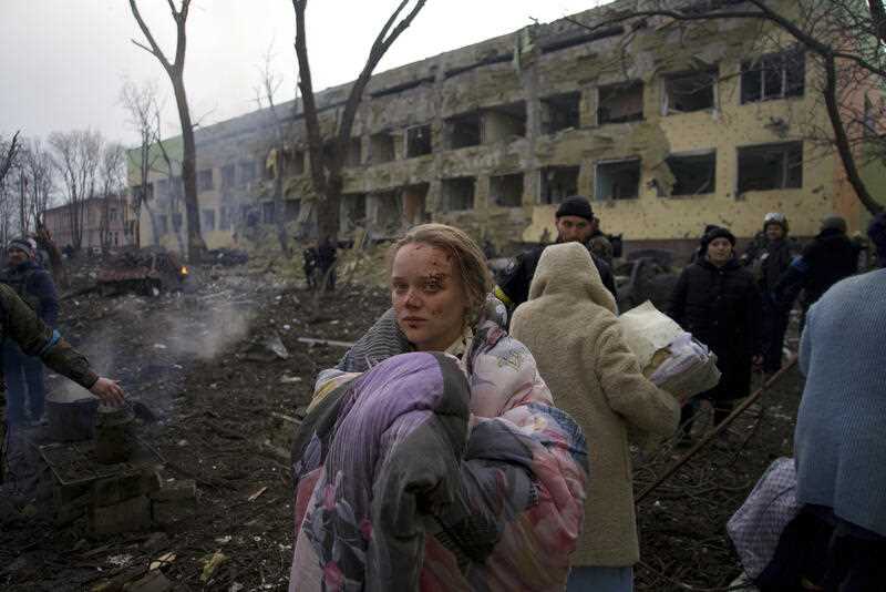 An injured pregnant woman stands outside a maternity hospital that was damaged by shelling in Mariupol, Ukraine, Wednesday, March 9, 2022
