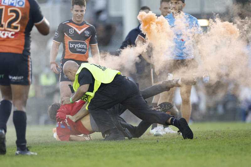 A pitch invader carrying a flare is tackled by security during the Round 5 NRL match between the Cronulla Sharks and Wests Tigers at PointsBet Stadium in Sydney, Sunday, April 10, 2022.