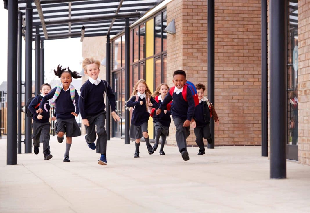 diverse group of primary school students in uniform running along pathway beside school building