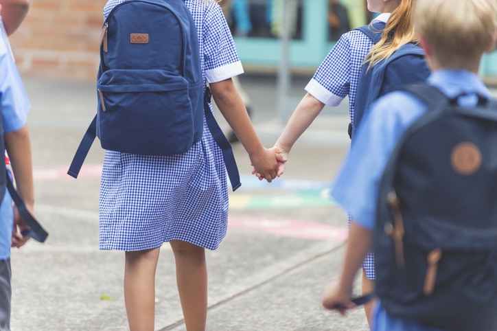 back view of 4 primary school children in blue uniforms wearing backpacks