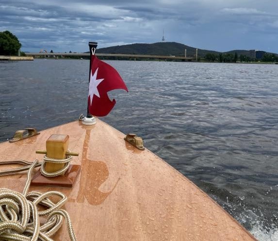 bow of wooden boat is seen gliding on Lake Burley Griffin on a rainy grey day