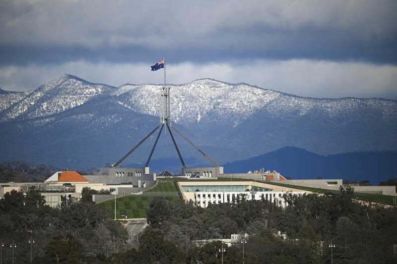 Parliament House is seen in front of snow-covered hills surrounding the Australian Capital Territory (ACT) in Canberra, Sunday, August 23, 2020. (AAP Image/Lukas Coch)