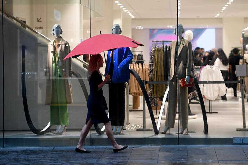 Peope are seen walking past shopfront windows in Sydney, Tuesday, March 29, 2022.