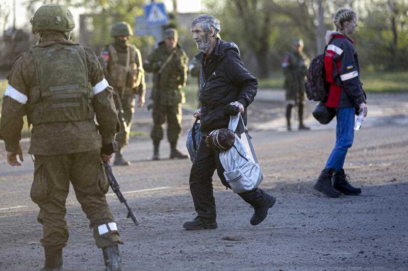 A man who left a shelter in the Azovstal steelworks walks to a bus between servicemen of Russian Army and Donetsk People's Republic militia in Bezimenne village in Ukraine's Mariupol district