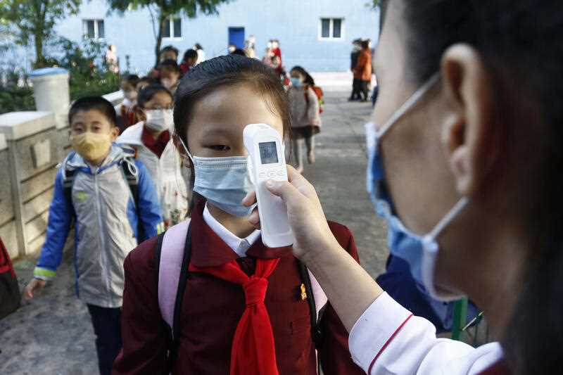 A teacher takes the body temperature of a schoolgirl to help curb the spread of the coronavirus before entering Kim Song Ju Primary School in Central District in Pyongyang, North Korea