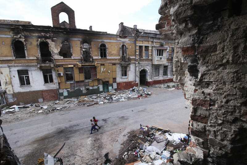 Children walk amid destroyed buildings in Mariupol which is Russian control in eastern Ukraine, Wednesday, May 25, 2022
