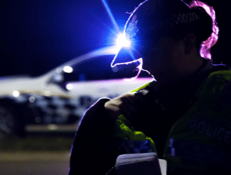 female police officer silhouetted at night against white police car in background