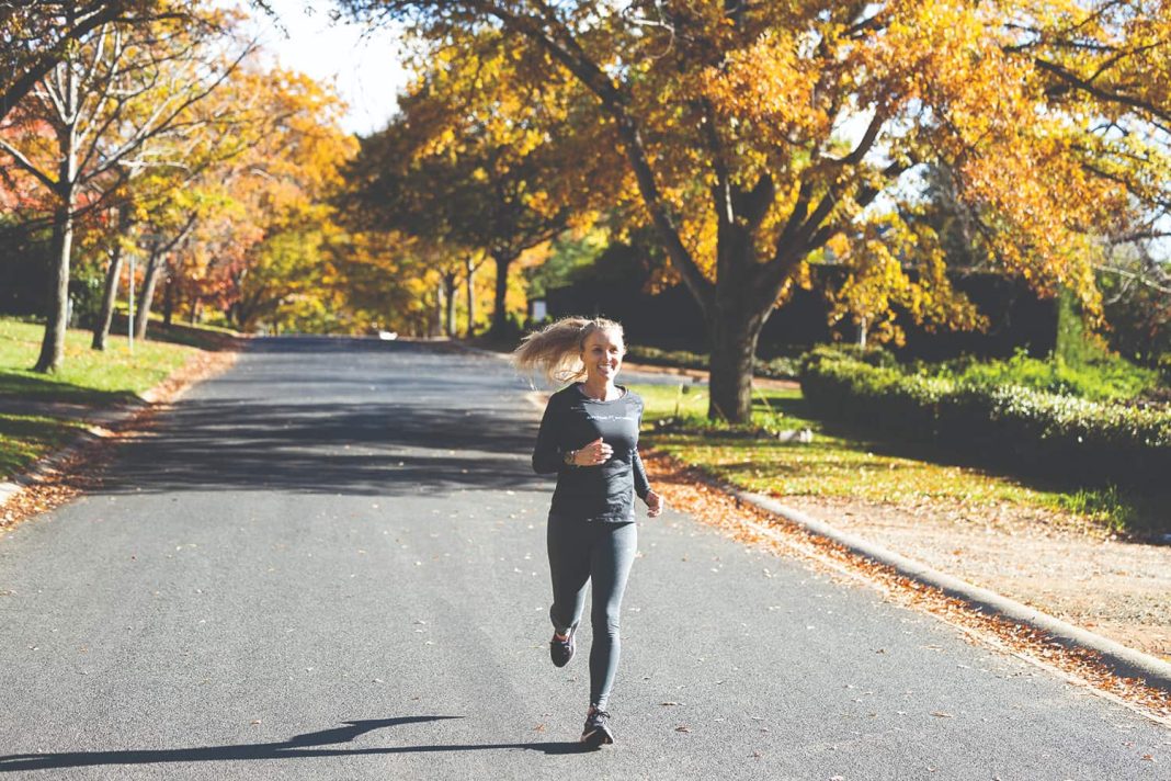 woman with blond ponytail jogging down leafy Canberra street in autumn