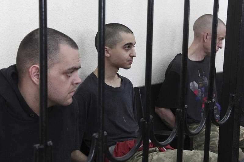 Two British citizens Aiden Aslin, left, and Shaun Pinner, right, and Moroccan Saaudun Brahim, center, sit behind bars in a courtroom in Donetsk, in the territory which is under the Government of the Donetsk People's Republic control, eastern Ukraine
