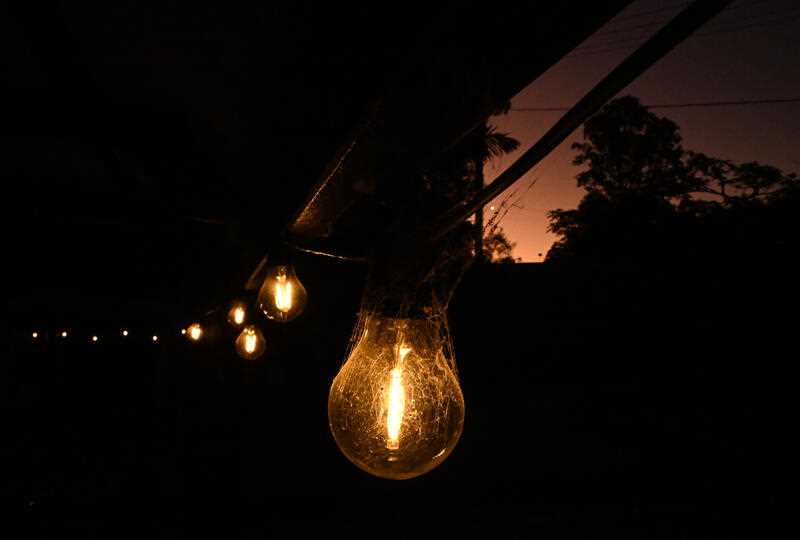 A string of electric light bulbs lit and hanging from a balcony at a house