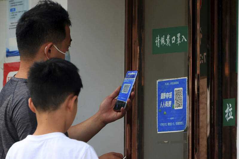 A man wearing a face mask scans a QR code for a health monitoring app to enter a shop in Zhengzhou in central China's Henan Province, Friday, June 17, 2022.